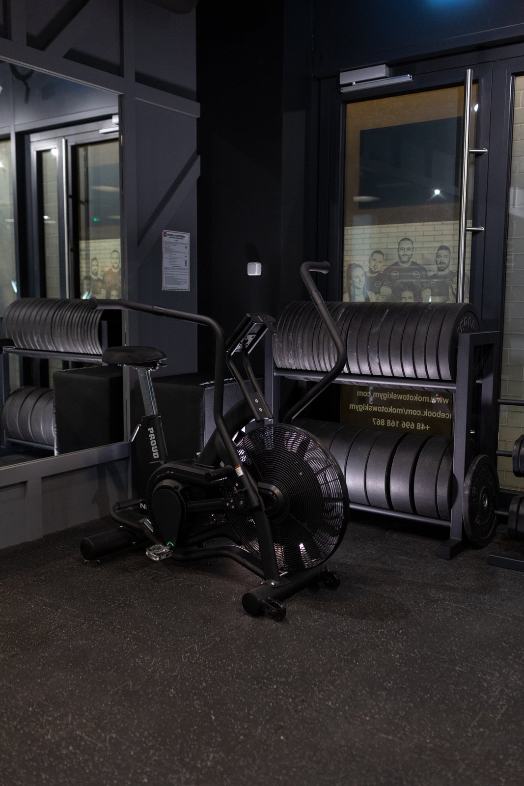 Stojak z talerzami olimpijskimi i rower treningowy na sali fitness